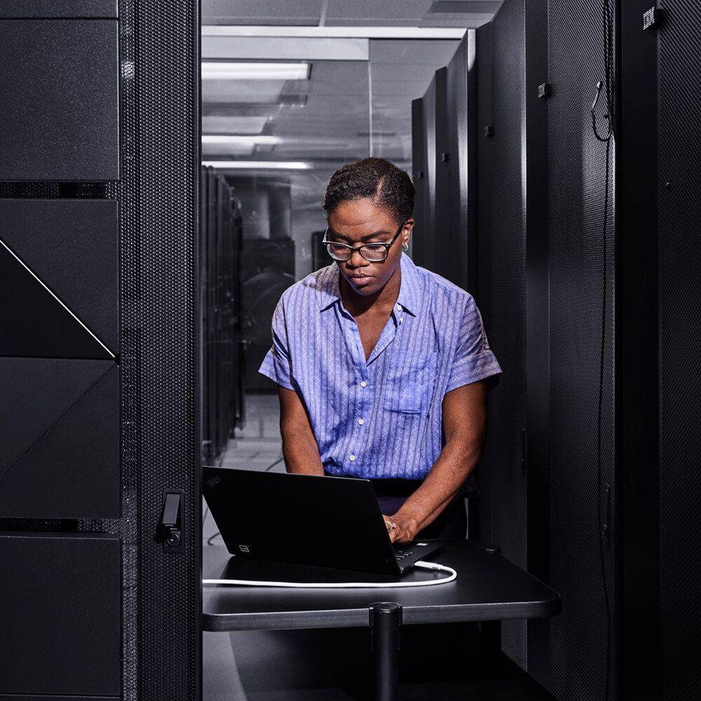 portait of person in server room at laptop